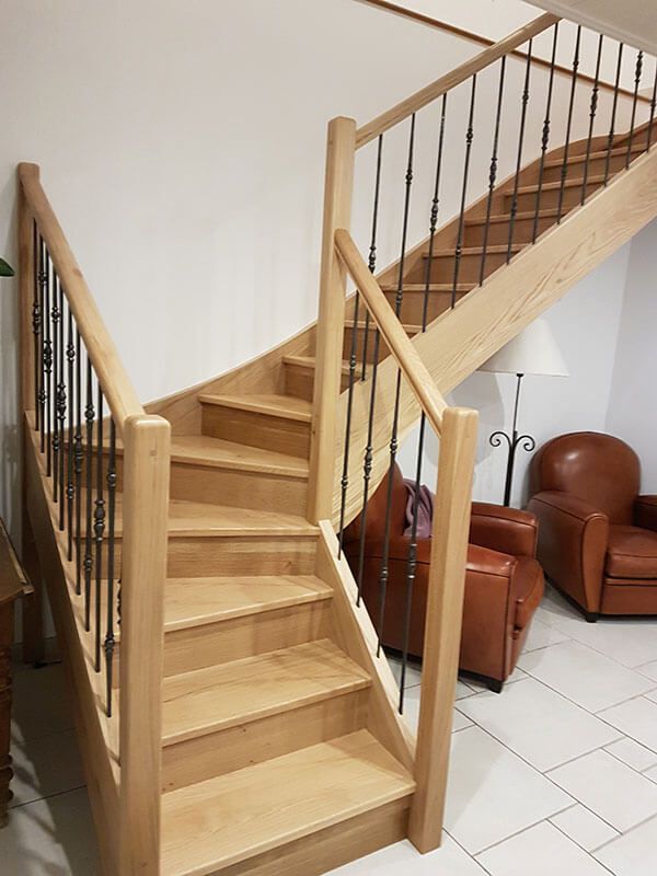 Escalier intérieur en bois avec rampe en métal à côté de fauteuils en cuir marron et d'un sol carrelé blanc