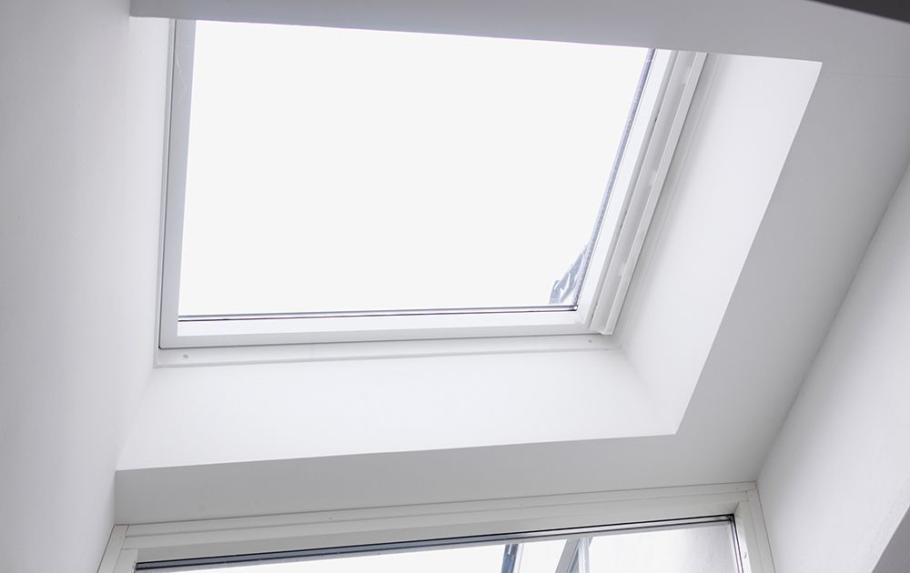 Fenêtre de toit blanche encastrée dans un plafond incliné, laissant entrer une lumière naturelle éclatante.