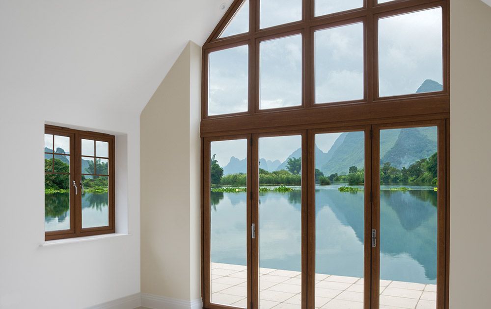 Chambre lumineuse avec de hautes fenêtres donnant sur un lac calme et des montagnes