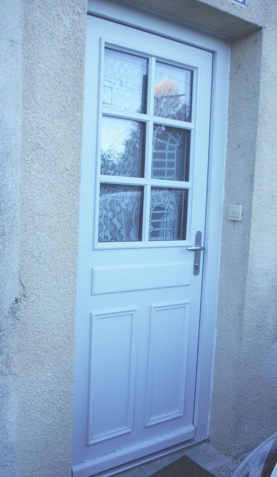Porte extérieure blanche à quatre vitres et poignée, encastrée dans un mur en stuc texturé.