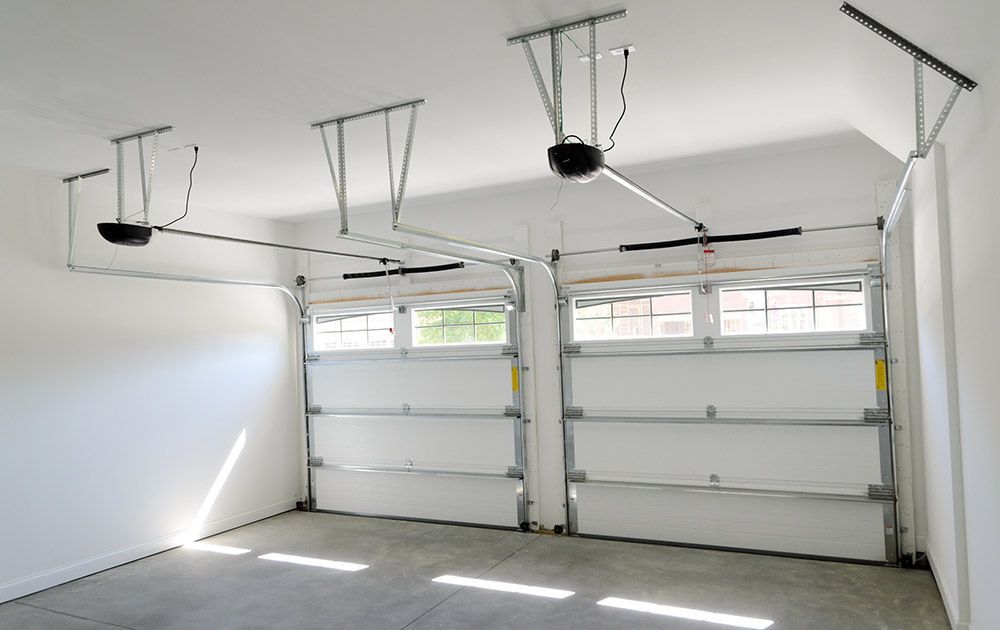 Garage blanc vide avec deux portes de garage sectionnelles et des étagères de rangement suspendues au plafond.