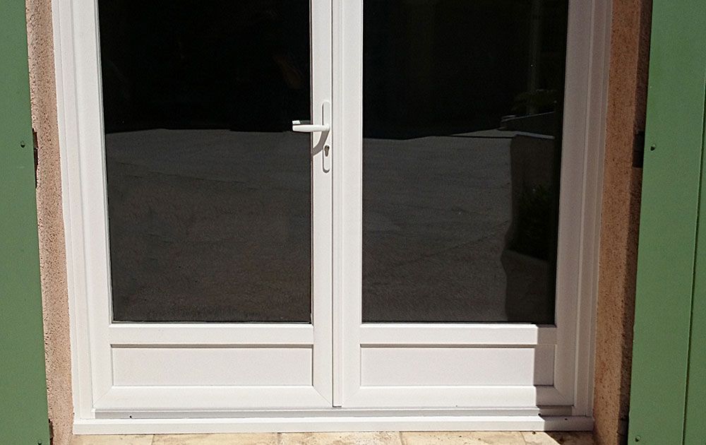 Fenêtre double blanche avec vitrage réfléchissant foncé, encastrée dans un mur beige, avec une bordure verte sur la droite.