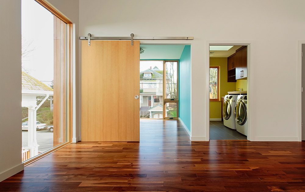 Pièce moderne vide avec parquet, portes ouvertes et vue sur une buanderie et un jardin.