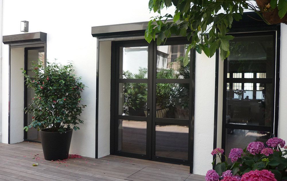 Entrée de maison moderne avec portes vitrées à cadre noir, plantes en pot et fleurs roses sur la terrasse