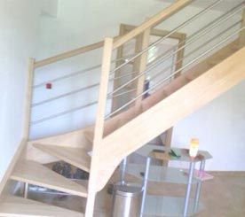 Escalier en bois clair avec rampes en métal et panneaux de verre dans un intérieur lumineux.