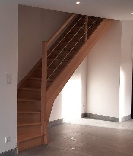 Escalier en bois avec rampes métalliques dans une pièce intérieure nue aux murs clairs et au sol carrelé