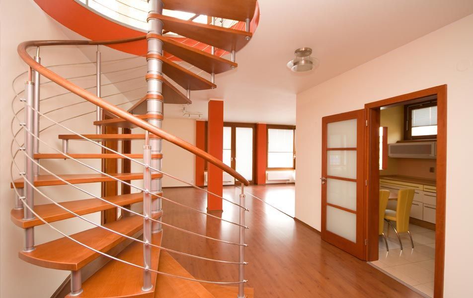 Intérieur moderne avec un escalier en bois incurvé, des planchers de bois franc et une porte ouverte sur une cuisine.
