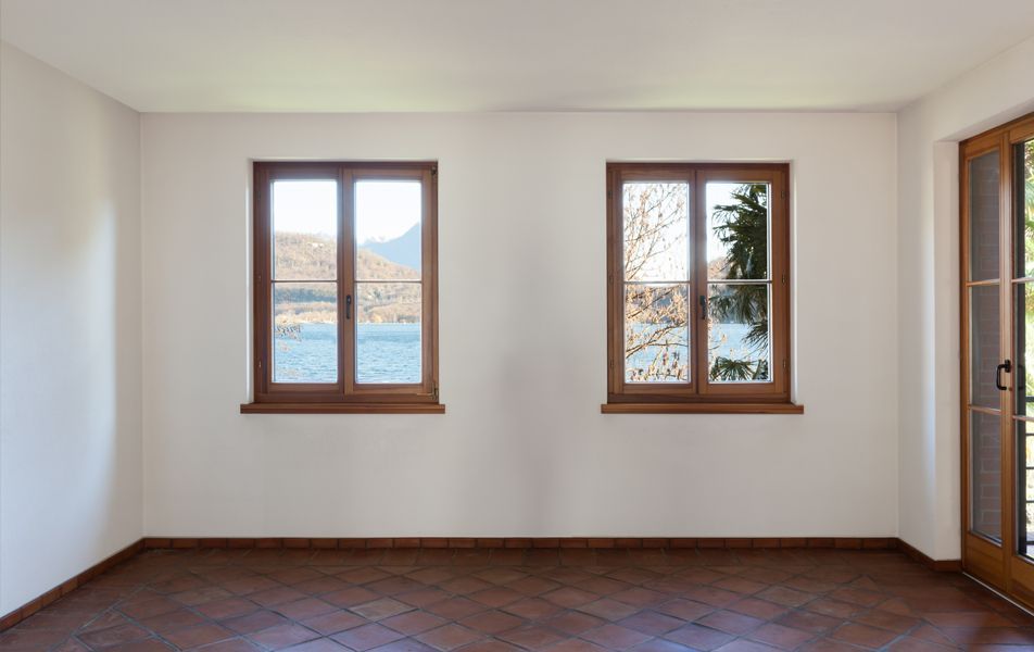 Pièce vide aux murs blancs, parquet et deux fenêtres donnant sur l'eau.