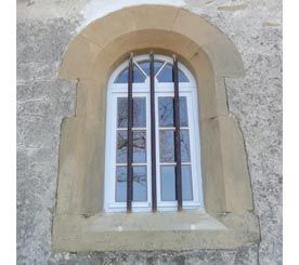 Fenêtre cintrée blanche encadrée de pierre beige sur un mur gris brut