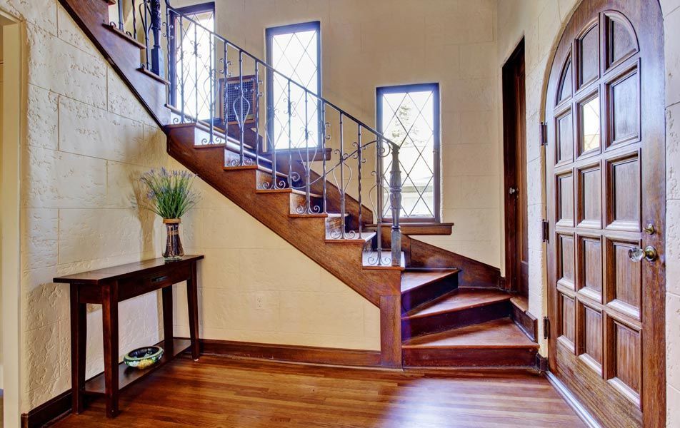 Hall d'entrée lumineux avec escalier en bois, porte cintrée et petite table avec des fleurs contre le mur.