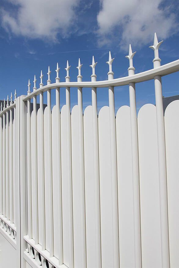 Clôture en métal blanc à embouts pointus se détachant sur un ciel bleu nuageux