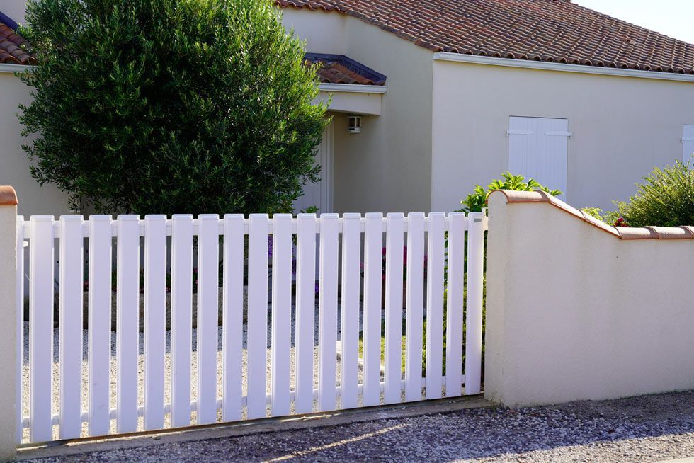 Portail blanc et mur en stuc devant une maison avec un arbre verdoyant.