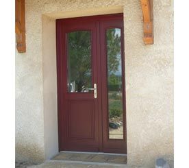Porte d'entrée bordeaux à panneaux de verre, encastrée dans un encadrement en stuc avec poutres en bois au-dessus.