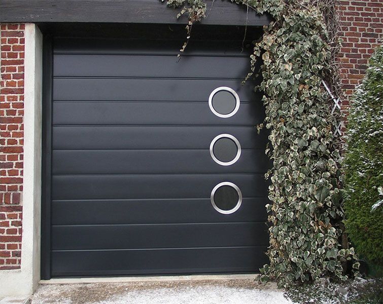 Porte de garage sombre ornée de trois cercles blancs, jouxtant un mur de briques recouvert de lierre