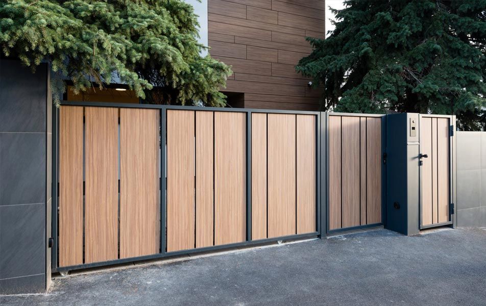 Portail moderne en bois et métal noir le long d'une allée bordée d'un bâtiment et d'arbres.