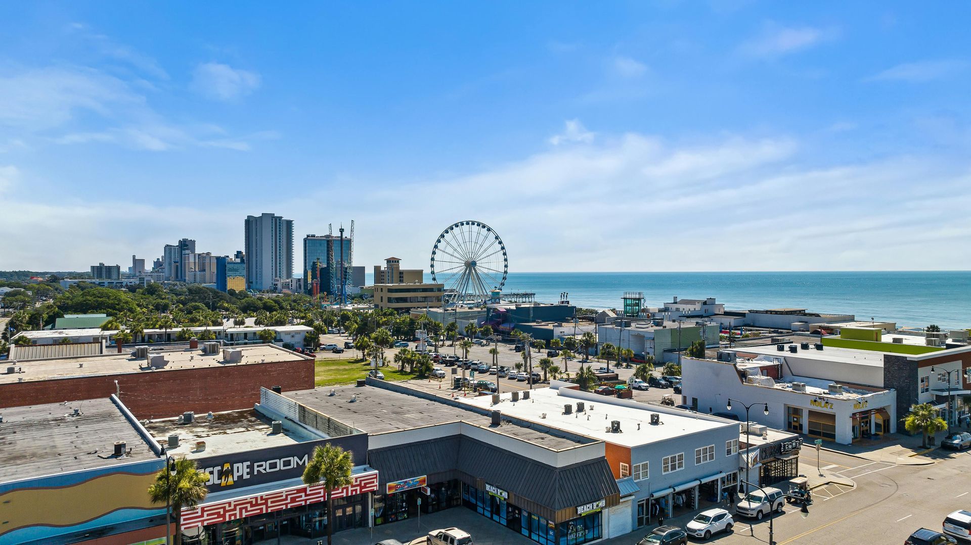 Buildings along the coast with a large Ferris wheel, skyline, and ocean under a blue sky.