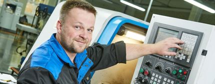 Techniker im blauen Hemd bedient ein Bedienfeld neben einer Maschine in einer Werkstatt