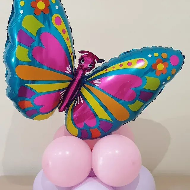 Un globo de mariposa colorido está sentado encima de globos rosados ​​y morados.