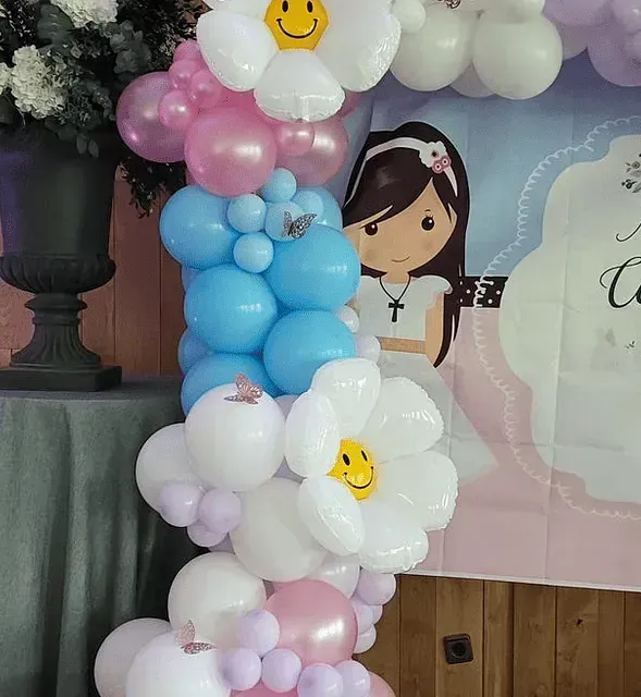 Una niña con un vestido blanco está detrás de un arco de globos.