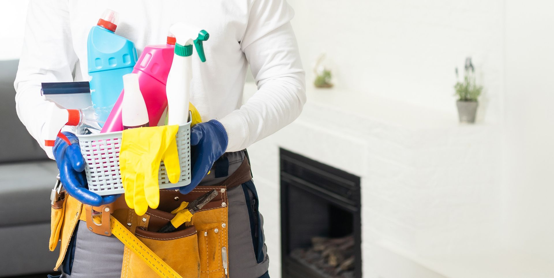 Persona sosteniendo suministros de limpieza, incluidas botellas y guantes, con una chimenea al fondo.