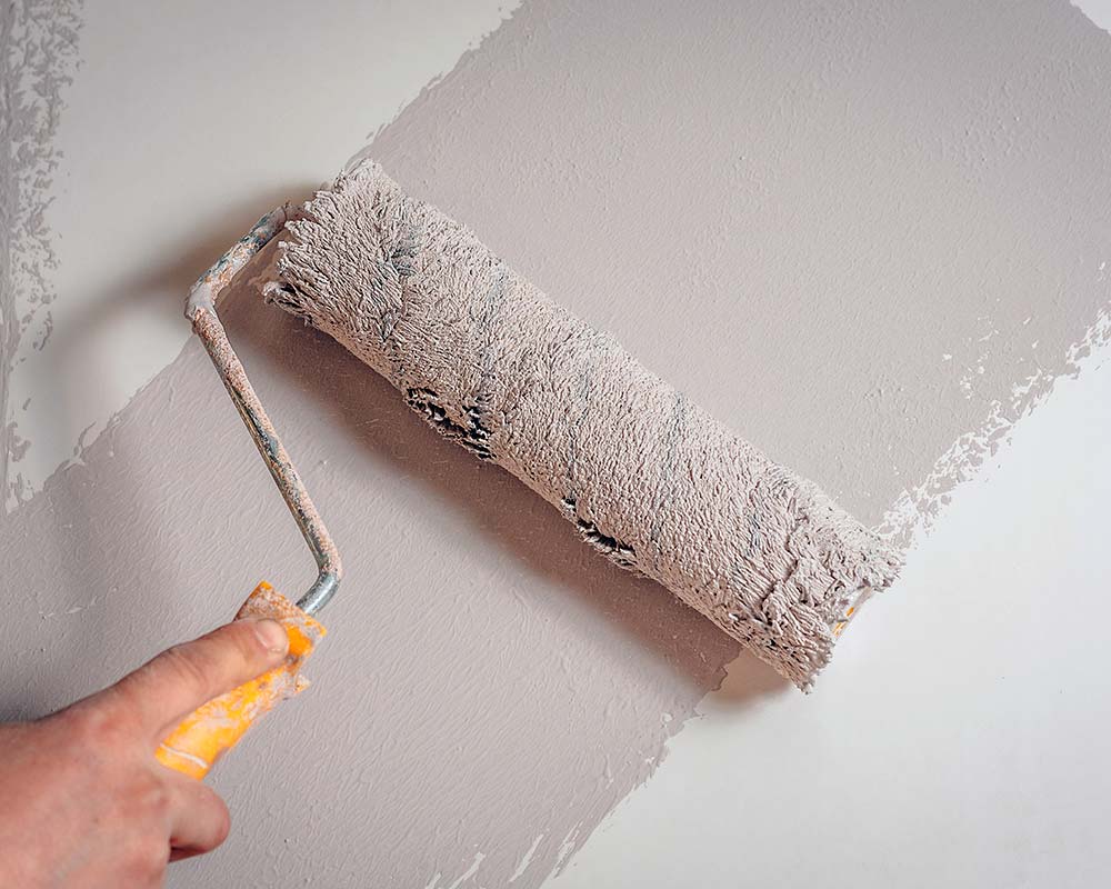 Rouleau appliquant de la peinture grise sur un mur
