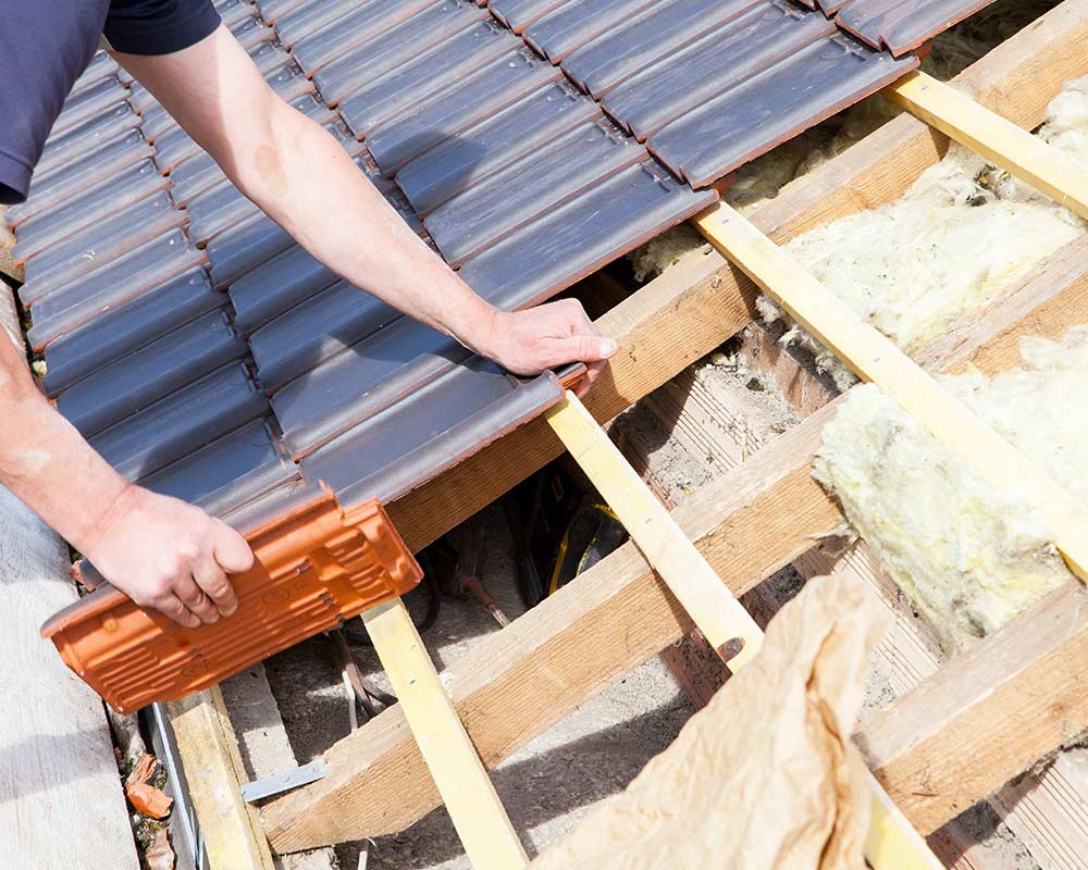 Main d'un ouvrier en train de poser une tuile sur un toit en rénovation