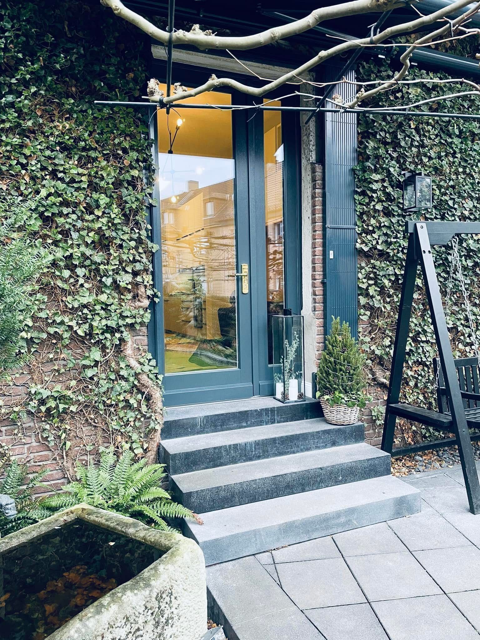 Eine Tür, zu der eine Treppe hinaufführt, ist von Efeu umgeben.