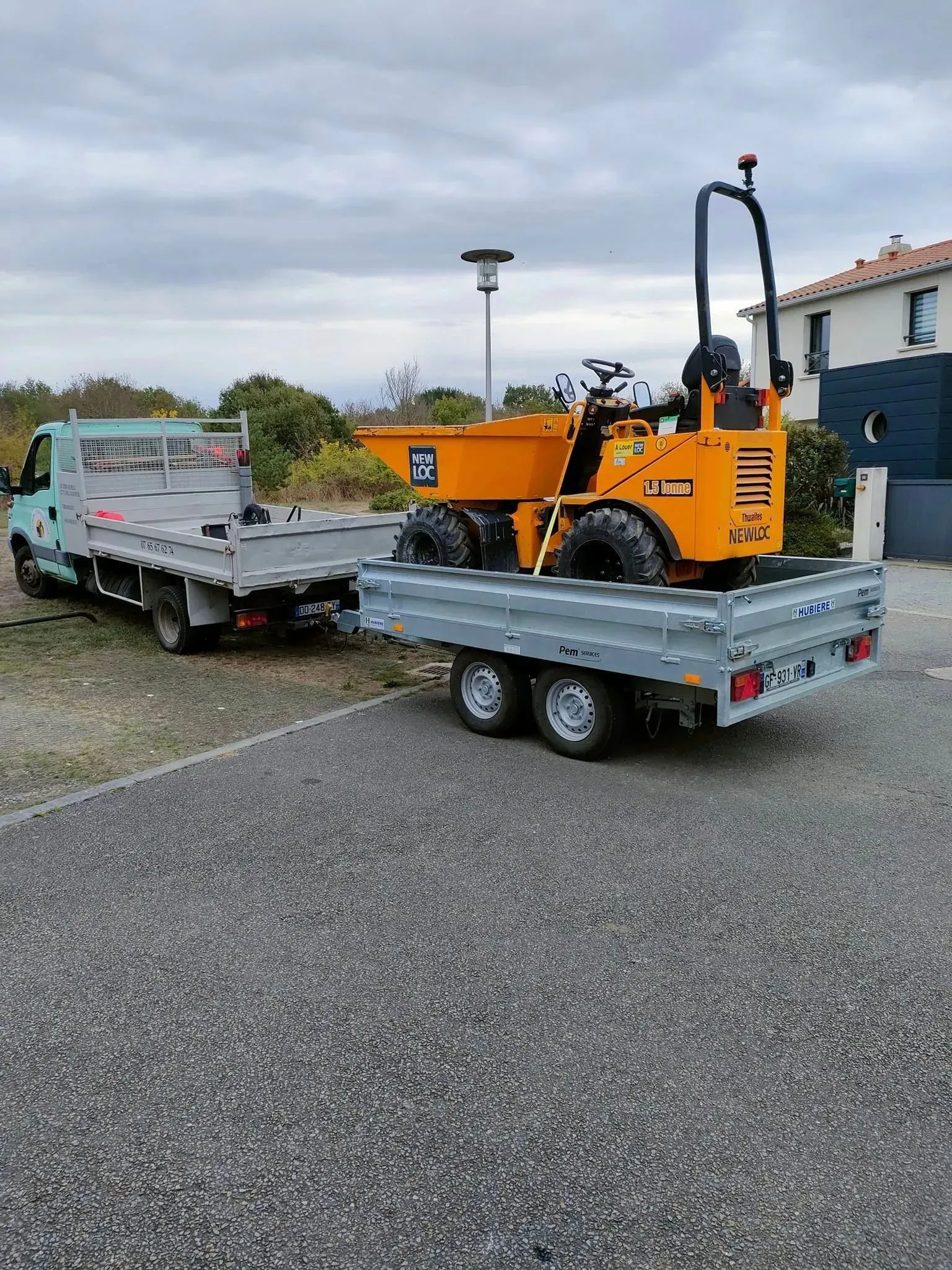 Camion tractant une remorque avec une mini-benne orange sur un terrain gravillonné gris. 