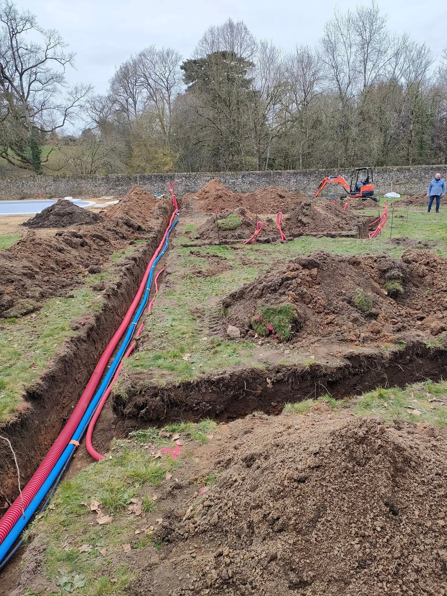 Des tranchées avec des tuyaux rouges et bleus dans un champ herbeux ; des travaux de construction sont en cours