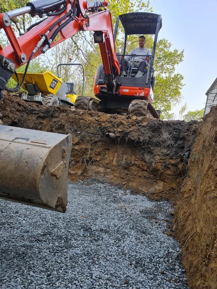 Une excavatrice creuse une tranchée remplie de gravier. Une personne manœuvre l'engin à l'extérieur.