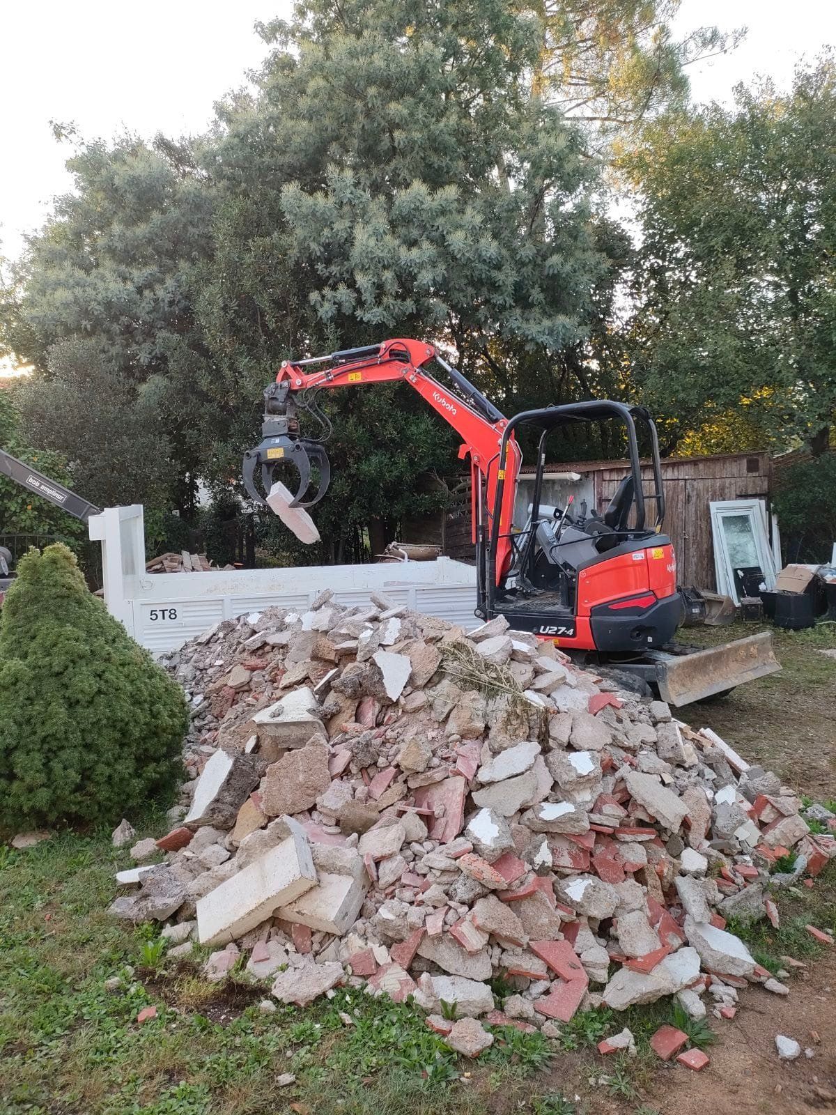 Une pelle mécanique rouge utilise une pince pour déplacer des débris d'un chantier de démolition.