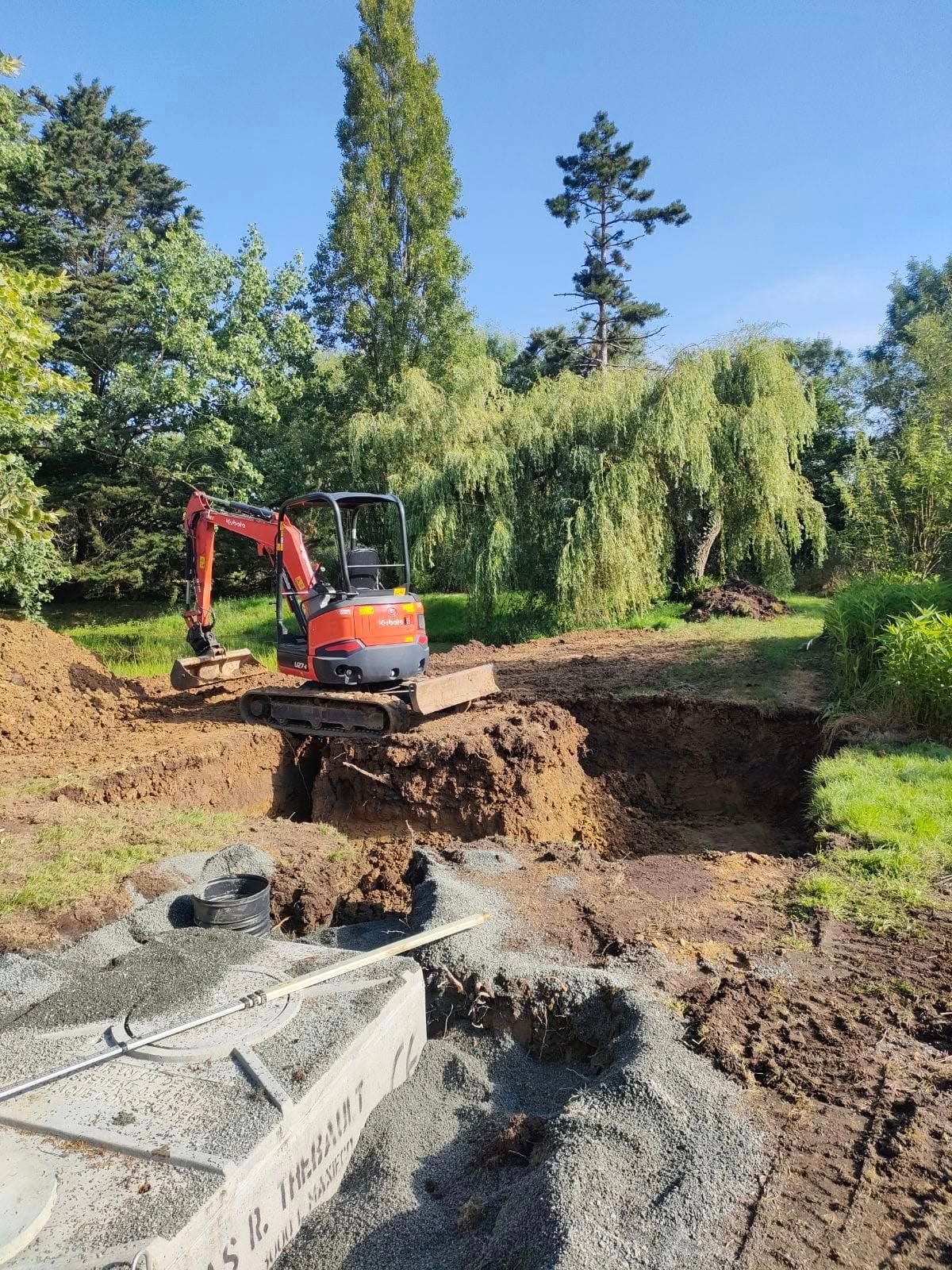 Une mini-pelle creuse un trou dans une zone herbeuse, en prévision d'un chantier