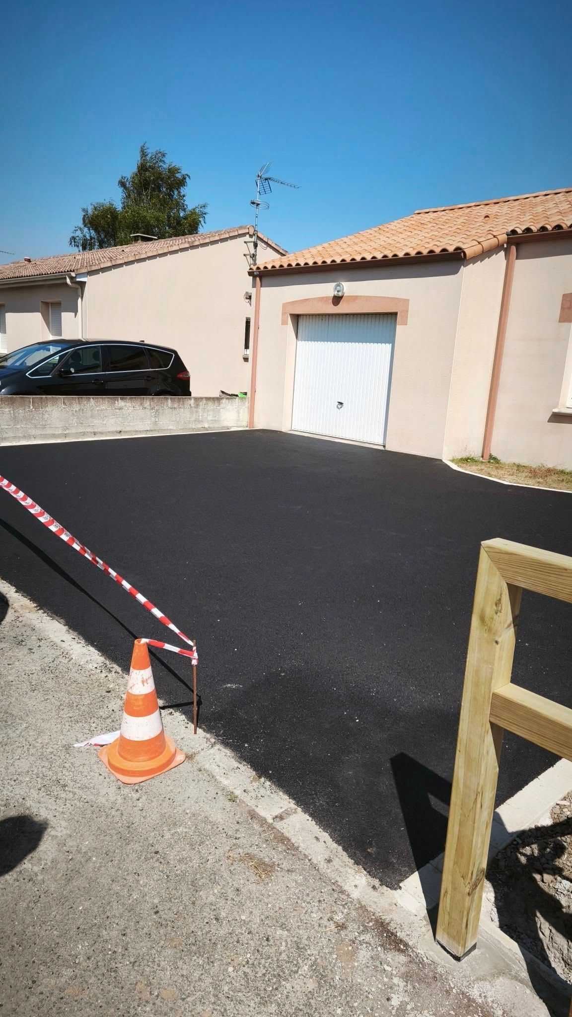 Allée en asphalte noir fraîchement pavée devant des maisons aux couleurs claires, sous un ciel bleu azur.