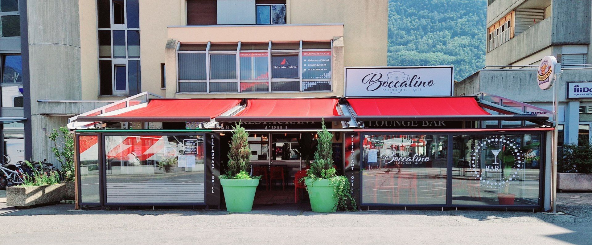 Un restaurant avec un auvent rouge et des plantes en pot devant lui