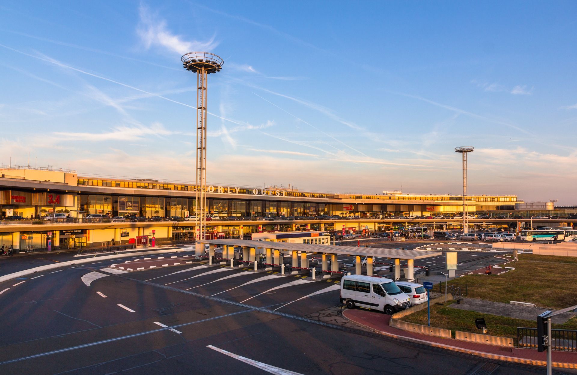 Extérieur de l'aéroport avec une tour, un parking et plusieurs voitures.