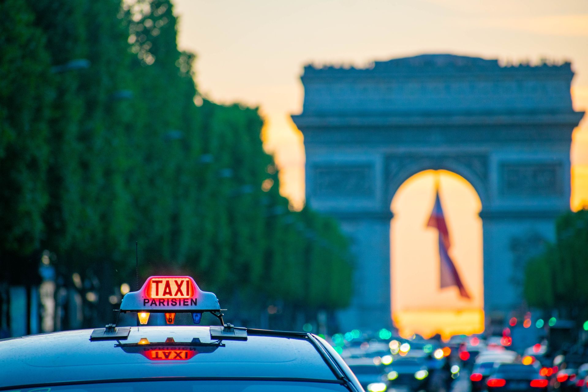Taxi avec panneau allumé roulant vers l'Arc de Triomphe à Paris au coucher du soleil.