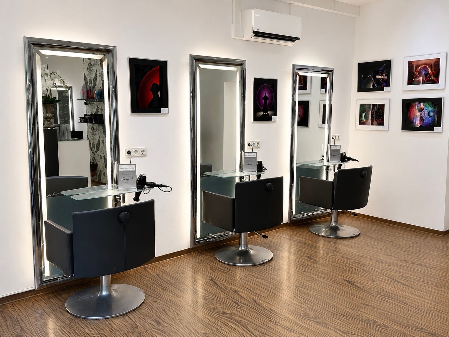 Moderner Friseursalon mit drei schwarzen Friseurstühlen, Spiegeln und gerahmter Wandkunst an weißen Wänden.