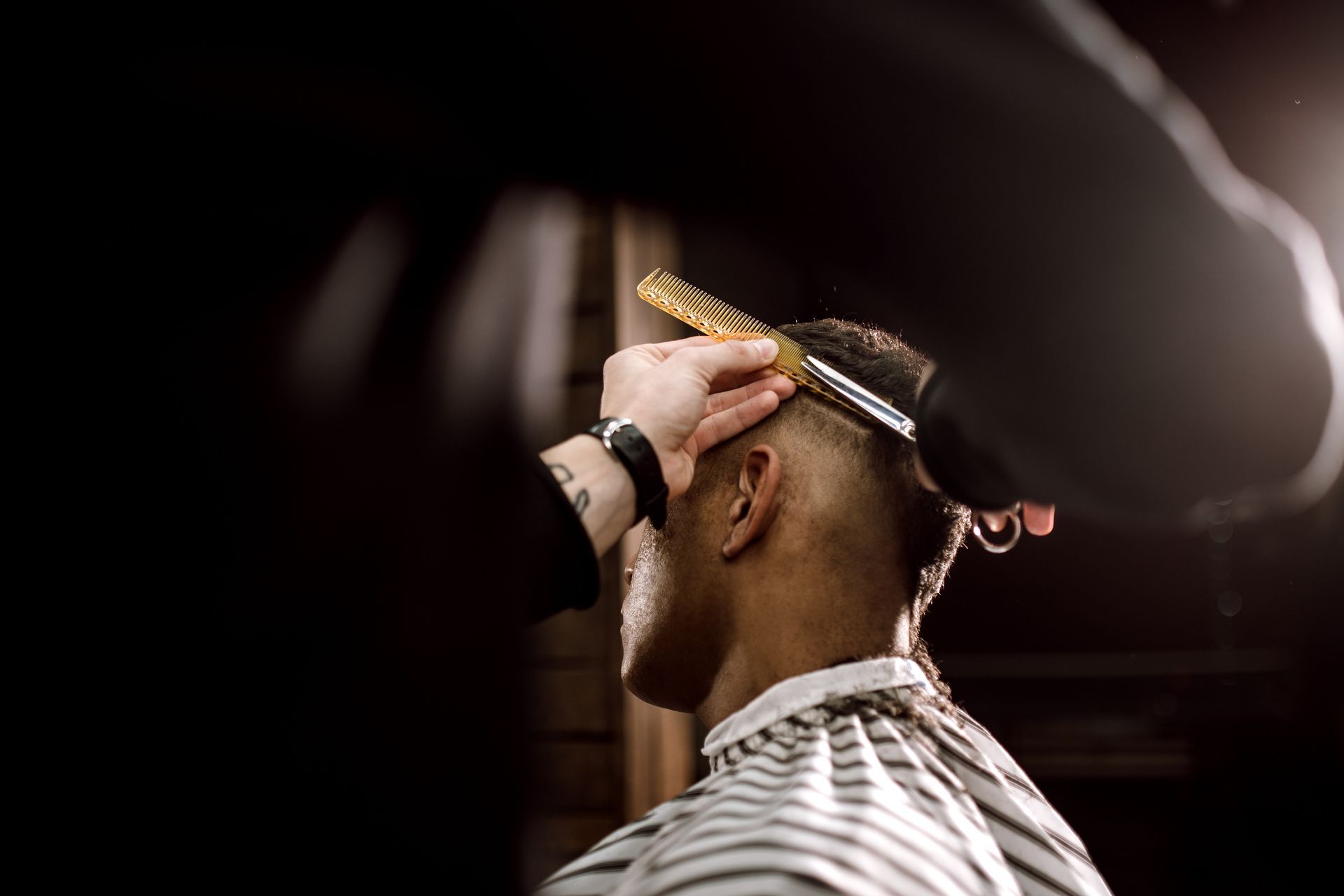 Ein Friseur stutzt einem Kunden in einem schwach beleuchteten Friseursalon mit Haarschneidemaschine und Kamm die Haare.