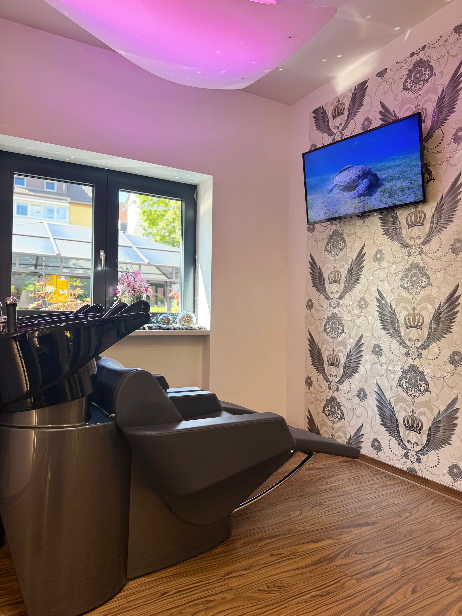 Stilvolle Lounge mit schwarzen Stühlen, violetten Deckenleuchten, Fernseher an der Wand und Fenster