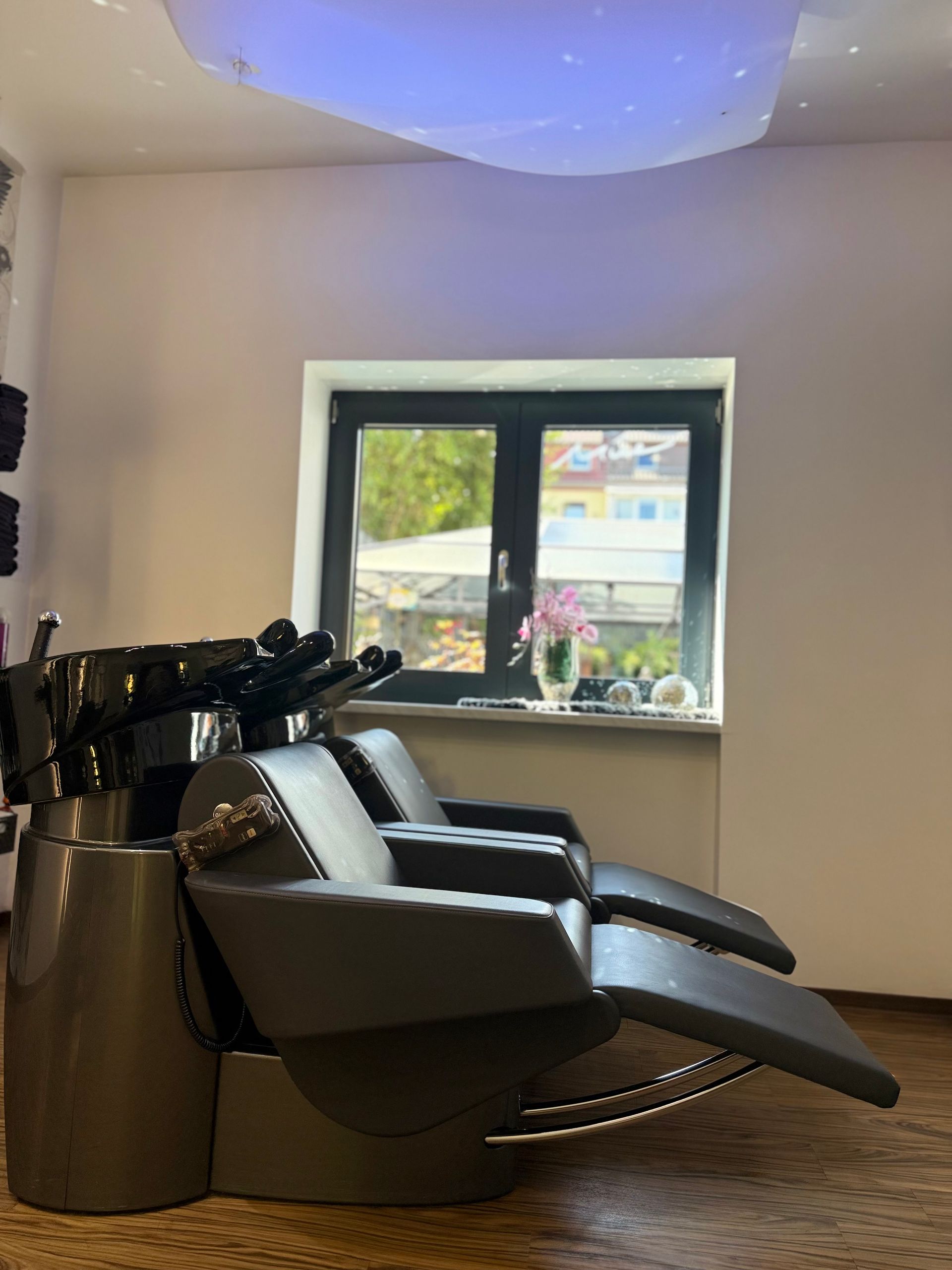 Salon mit schwarzen, zurückgelehnten Waschstühlen, einer geschwungenen Deckenleuchte und Blick nach draußen durch ein Fenster
