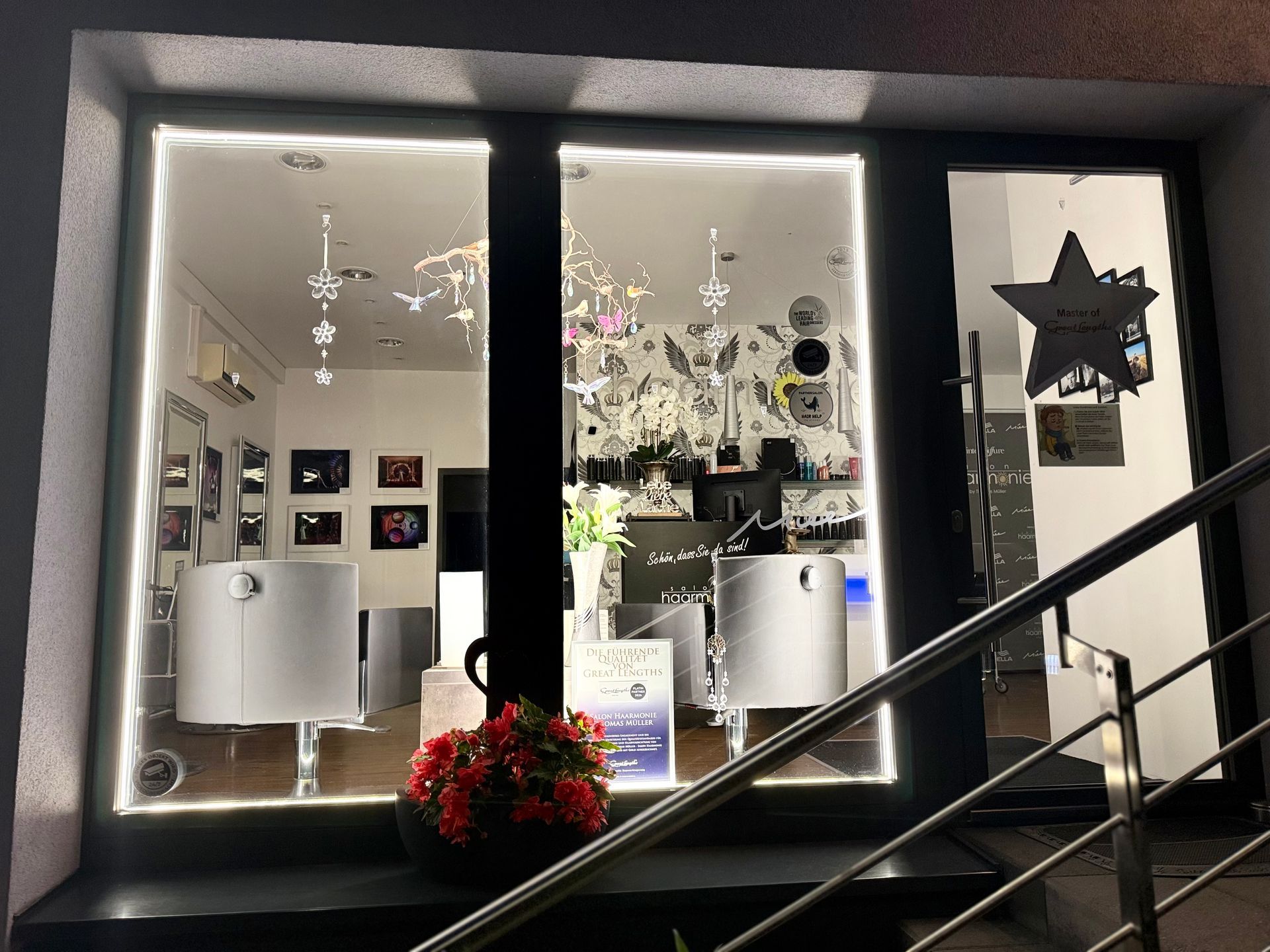 Schaufensterdekoration mit Hängelampen, gerahmten Bildern und roten Blumen am Eingang.