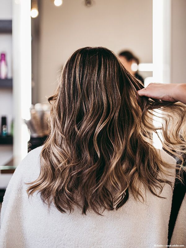 Rückansicht von schulterlangem, gewelltem, braunem Haar, das vor einem Salonspiegel gestylt wird