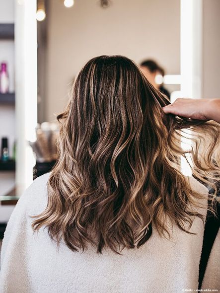 Frau mit welligem braunem Haar, die sich in einem Salon die Haare schneiden lässt, von hinten betrachtet