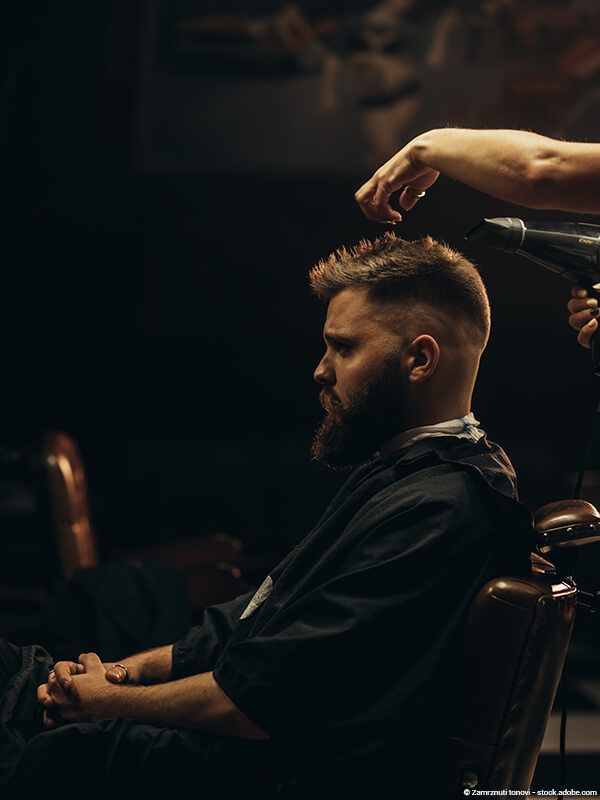 Ein Barbier stylt einem Mann die Haare in einem schwach beleuchteten Friseursalon.