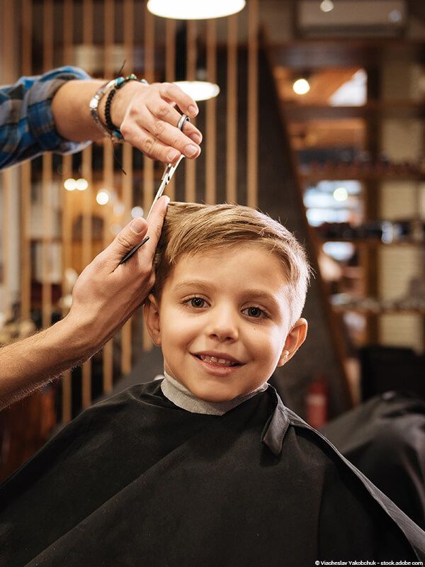 Ein Kind lässt sich in einem Friseursalon die Haare schneiden und lächelt, während die Schere die Haare stutzt.