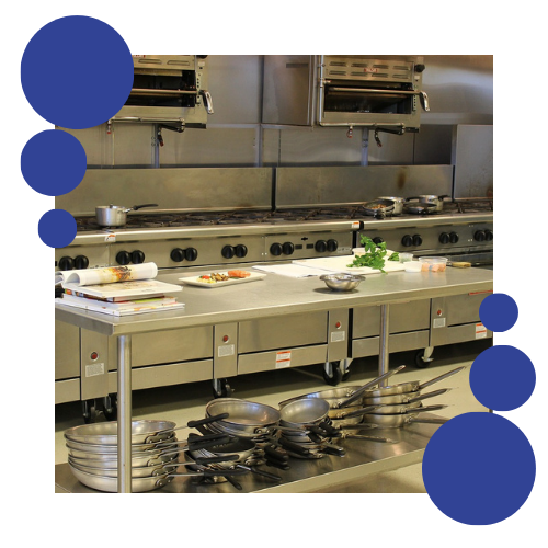 Una cocina con una larga mesa de acero inoxidable llena de ollas y sartenes.