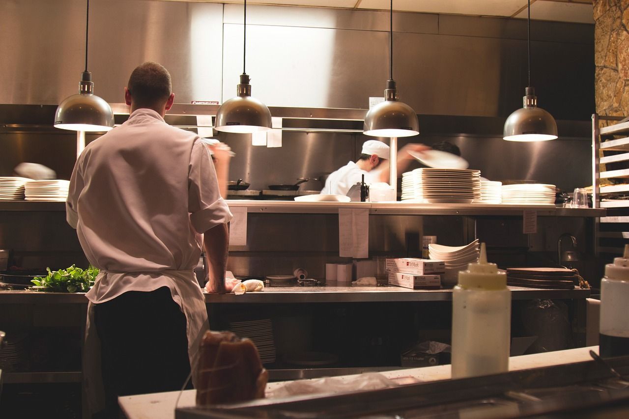 Un hombre con delantal está de pie en una cocina con otros chefs.