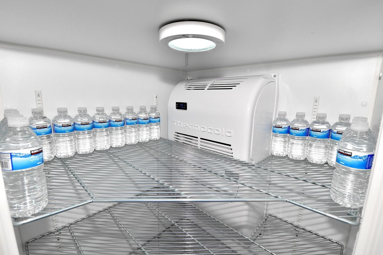 Un refrigerador lleno de botellas de agua y un ventilador.