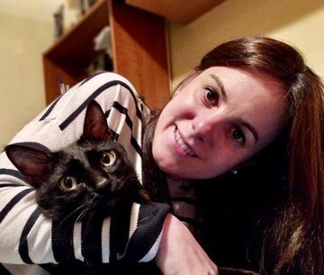 Mujer sonriendo, sosteniendo cerca un gato negro, ambos mirando a la cámara.