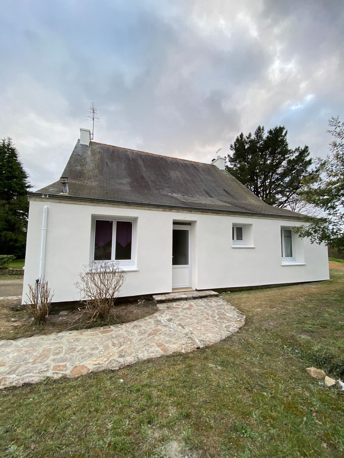 Petite maison blanche avec un toit foncé, une porte d'entrée, des fenêtres et un chemin de gravier dans une cour herbeuse